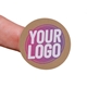 Kraft circle label sticker with a custom purple and white logo, shown on a fingertip. The natural brown background of the label gives a rustic and eco-friendly appearance, ideal for personalised packaging.