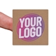 Kraft square label sticker with a custom purple and white logo, shown on a fingertip. The natural brown background of the label gives a rustic and eco-friendly appearance, ideal for personalised packaging