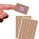 Hand holding a rectangular kraft label with a ribbed texture and a personalised design featuring the text Your Logo in bold pink and white. Behind it, sheets of similar kraft labels are displayed, showing a set of four per sheet.