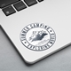 A circular Summer Camping Exploring World vinyl sticker on a silver laptop. The design features a black and white mountain and forest illustration, with the text encircling the image. It includes phrases like Adventure Outdoors and Green Forest Tourism.