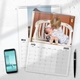 Two A4 photo calendars for 2025, opened to May and July. The July calendar features a child kissing a baby on a white bench. A smartphone and pen are placed next to the calendars on a white desk, with space for notes in the month grids.