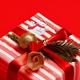 Red and white striped gift box wrapped with a red ribbon, decorated with a gold bauble and greenery. A personalised snowman sticker with a red scarf and Santa hat reads 