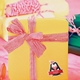 Yellow gift box wrapped with a red and white striped ribbon, featuring a personalised penguin Christmas sticker labelled 