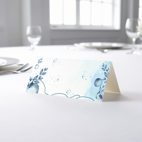 blank wedding place card with an elegant design printed on folded white cardstock, ready to write your names. Placed on a table set for a formal event, with plates, cutlery, and wine glasses in the softly blurred background.