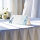 blank wedding place card printed with an elegantdesign on folded white cardstock ready to write your names on. Displayed on a table with a flowing white tablecloth, with soft natural light and white roses in the background.