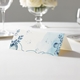 wedding place card with an elegant design on folded white cardstock ready to write your name on. Displayed on a white tablecloth with wine glasses, plates, and a floral centrepiece in the softly blurred background.