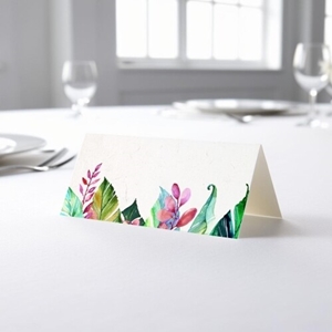 blank wedding place card with an elegant design printed on folded white cardstock, ready to write your names. Placed on a table set for a formal event, with plates, cutlery, and wine glasses in the softly blurred background.