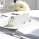 blank wedding place card with elegant design on folded white cardstock. Placed on a white plate with silver cutlery and a neatly folded napkin, with soft-focus white flowers in the background.