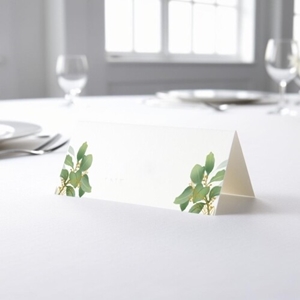 blank wedding place card with an elegant design printed on folded white cardstock, ready to write your names. Placed on a table set for a formal event, with plates, cutlery, and wine glasses in the softly blurred background.