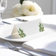 blank wedding place card with elegant design on folded white cardstock. Placed on a white plate with silver cutlery and a neatly folded napkin, with soft-focus white flowers in the background.