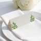 wedding place card with an elegant design on folded white cardstock, ready to write your names on. Positioned on a neatly folded white napkin atop a white plate, with a soft-focus white rose in the background.