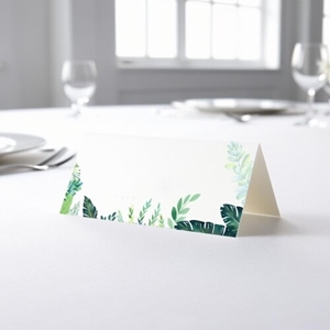 blank wedding place card with an elegant design printed on folded white cardstock, ready to write your names. Placed on a table set for a formal event, with plates, cutlery, and wine glasses in the softly blurred background.