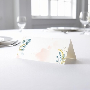 blank wedding place card with an elegant design printed on folded white cardstock, ready to write your names. Placed on a table set for a formal event, with plates, cutlery, and wine glasses in the softly blurred background.