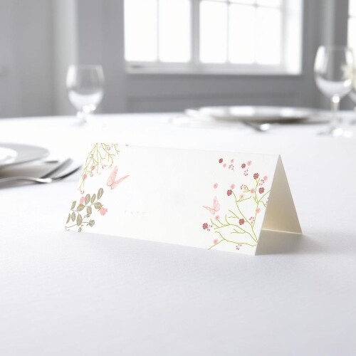 blank wedding place card with an elegant design printed on folded white cardstock, ready to write your names. Placed on a table set for a formal event, with plates, cutlery, and wine glasses in the softly blurred background.