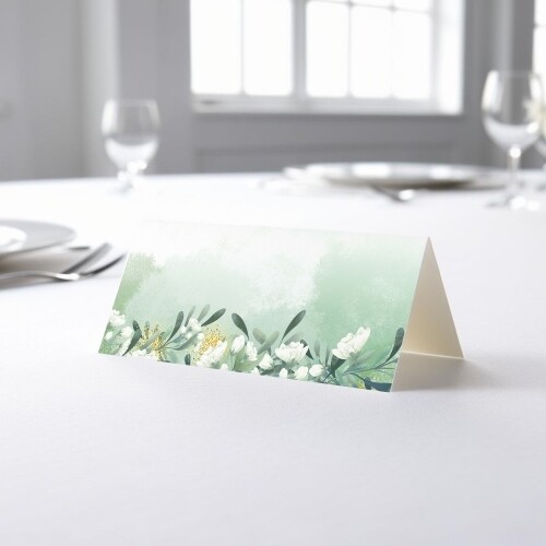 blank wedding place card with an elegant design printed on folded white cardstock, ready to write your names. Placed on a table set for a formal event, with plates, cutlery, and wine glasses in the softly blurred background.