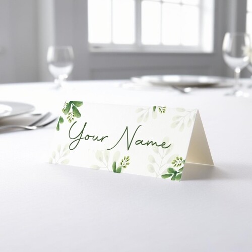 Personalised wedding place card with your name in elegant design on folded white cardstock. Placed on a table set for a formal event, with plates, cutlery, and wine glasses in the softly blurred background.