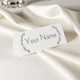 Personalised wedding place card with your name in elegant design on folded white cardstock. Set on a softly draped ivory tablecloth, creating a sophisticated and timeless look.