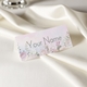 Personalised wedding place card with your name in elegant design on folded white cardstock. Set on a softly draped ivory tablecloth, creating a sophisticated and timeless look.