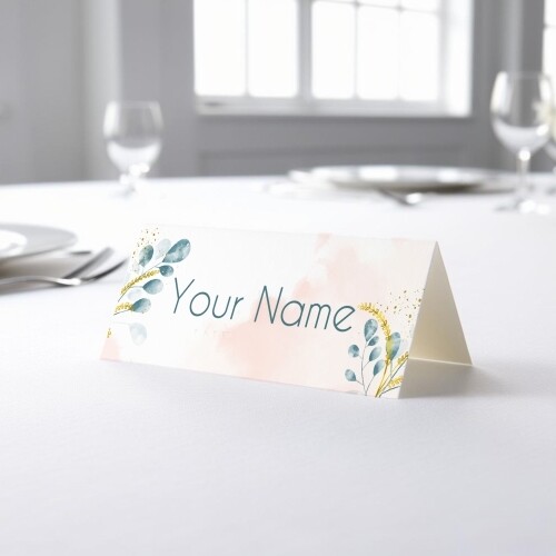 Personalised wedding place card with your name in elegant design on folded white cardstock. Placed on a table set for a formal event, with plates, cutlery, and wine glasses in the softly blurred background.