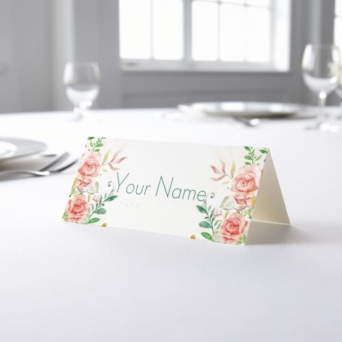 Personalised wedding place card with your name in elegant design on folded white cardstock. Placed on a table set for a formal event, with plates, cutlery, and wine glasses in the softly blurred background.