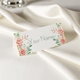 Personalised wedding place card with your name in elegant design on folded white cardstock. Set on a softly draped ivory tablecloth, creating a sophisticated and timeless look.