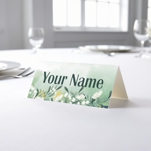 Personalised wedding place card with your name in elegant design on folded white cardstock. Placed on a table set for a formal event, with plates, cutlery, and wine glasses in the softly blurred background.