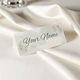 Personalised wedding place card with your name in elegant design on folded white cardstock. Set on a softly draped ivory tablecloth, creating a sophisticated and timeless look.