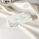 Personalised wedding place card with your name in elegant design on folded white cardstock. Set on a softly draped ivory tablecloth, creating a sophisticated and timeless look.